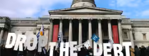 Crowd of people outside the London stock exchange carrying letters that spell out 'drop the debt'