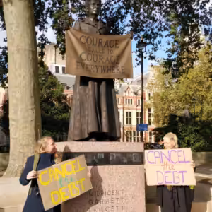 People holding 'Cancel the Debt' placards in front of the statue of suffragette Millicent Fawcett, who is holding a sign saying 'Courage calls to courage everywhere'.